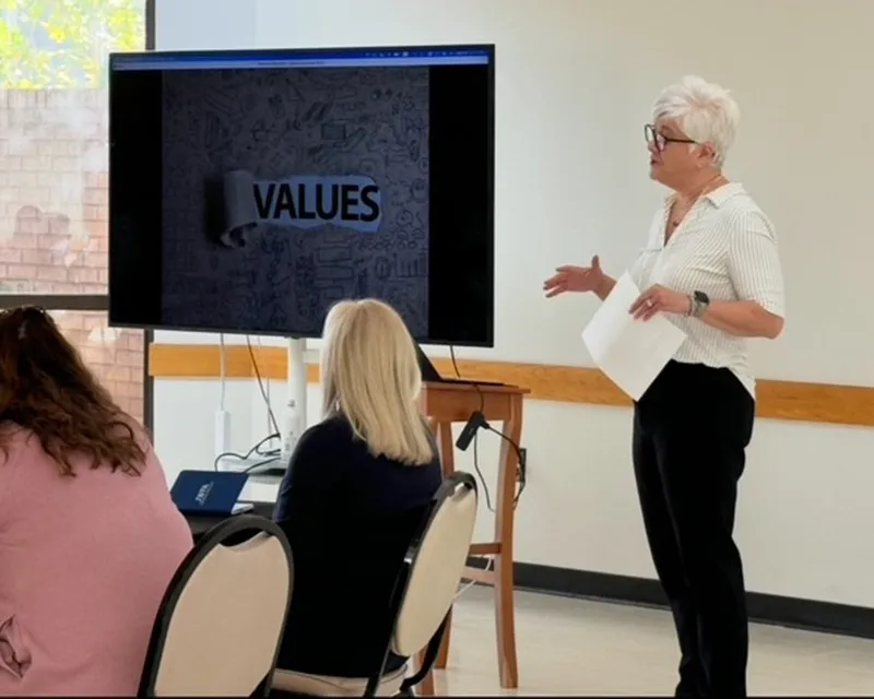 ACT2 woman speaking with presentation screen that says "Values"
