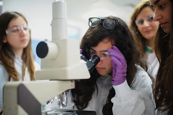 key-focus-areas girl looking through microscope wearing gloves and lab gear
