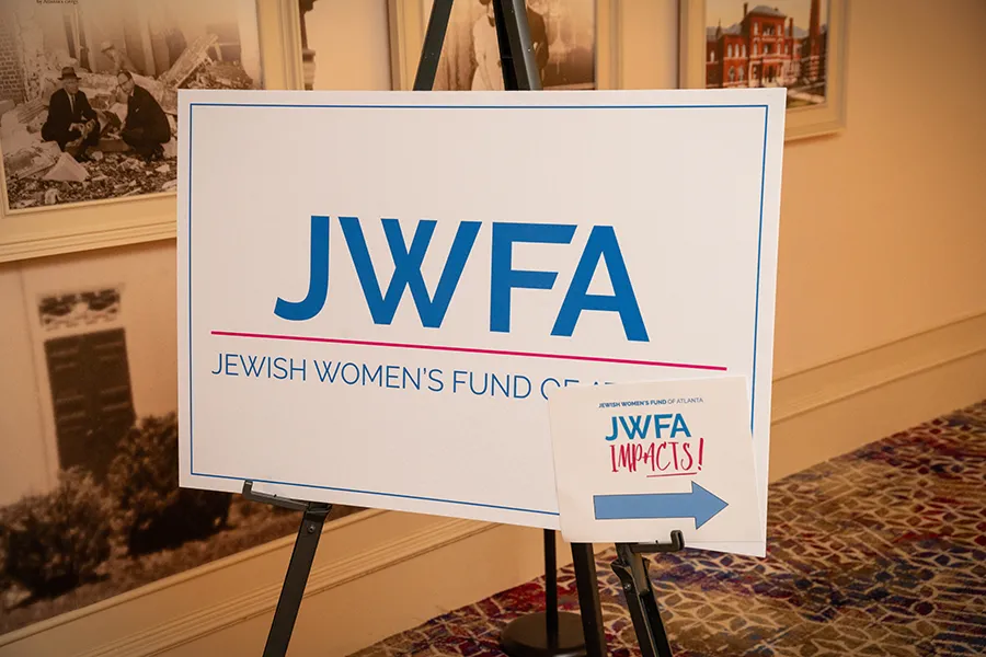 engagewithus a sign at a JWFA event with the logo and an arrow that says "JWFA IMPACTS!"